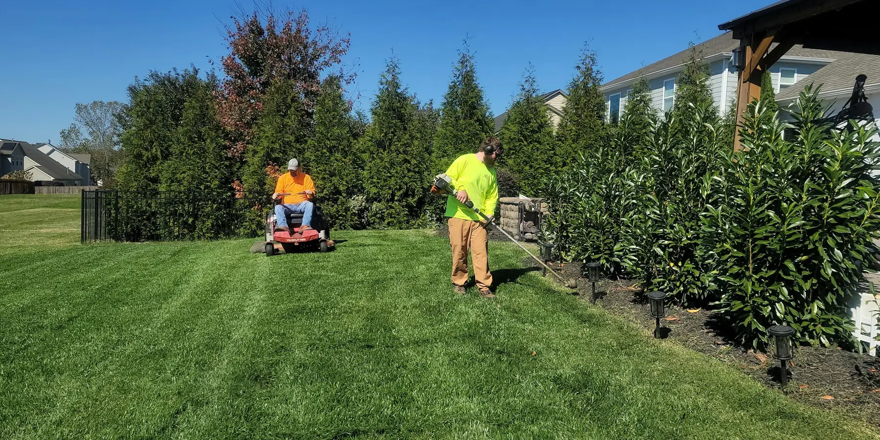 A two-man lawn crew mowing and trimming a residential property